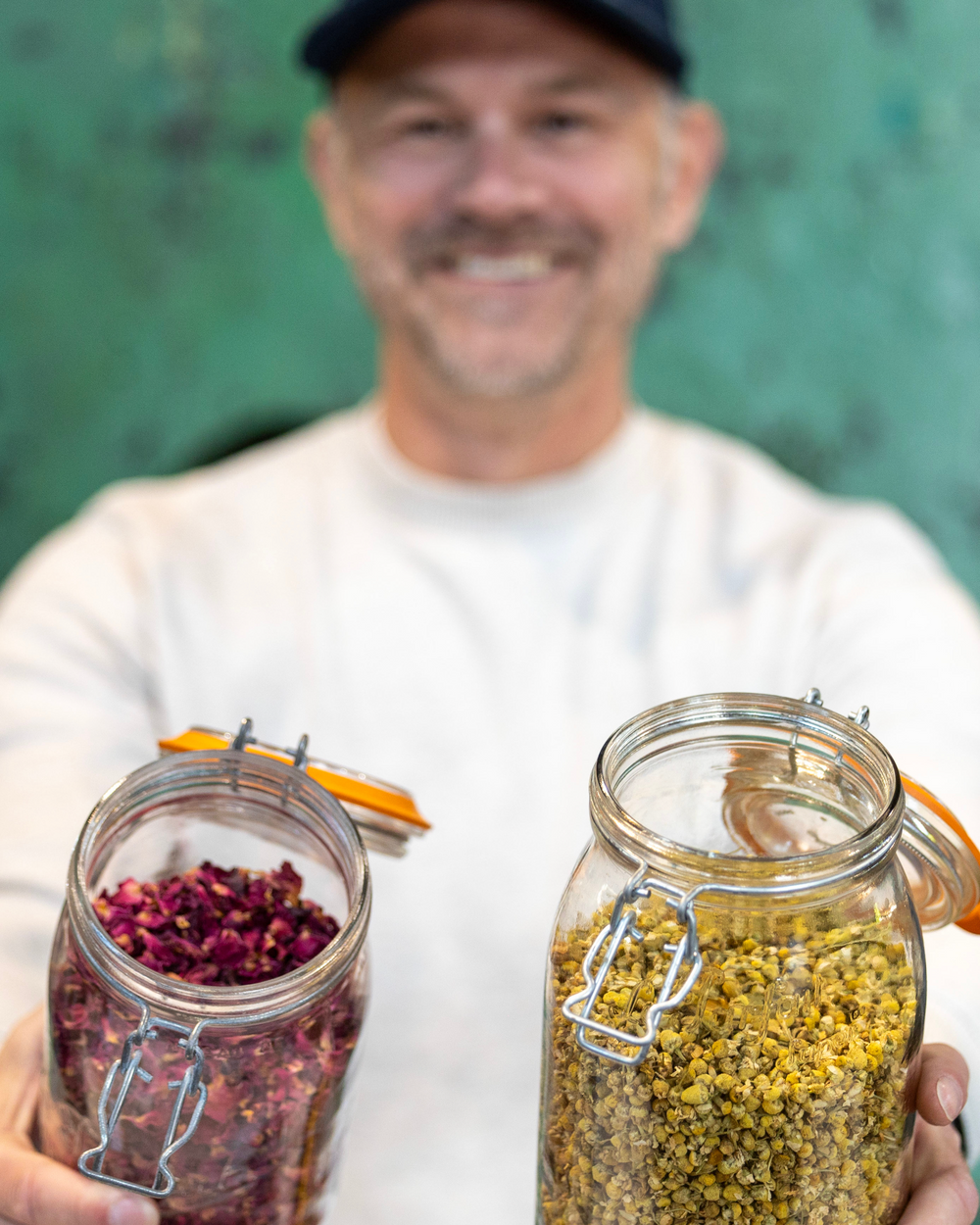 Ryan Sharp, founder, holding jars of rose petals and chamomile
